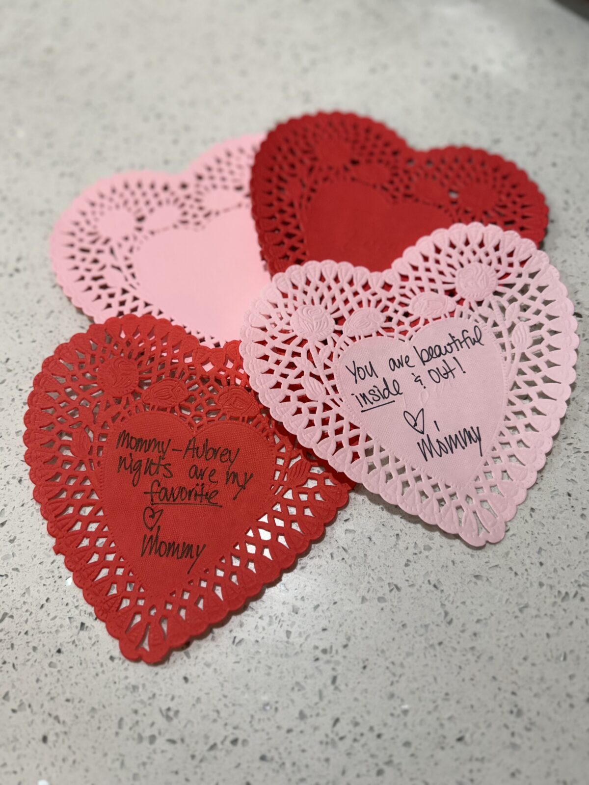 Three heart-shaped paper doilies with handwritten notes of love and appreciation from a mother to her child.