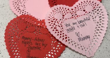 Three heart-shaped paper doilies with handwritten notes of love and appreciation from a mother to her child.